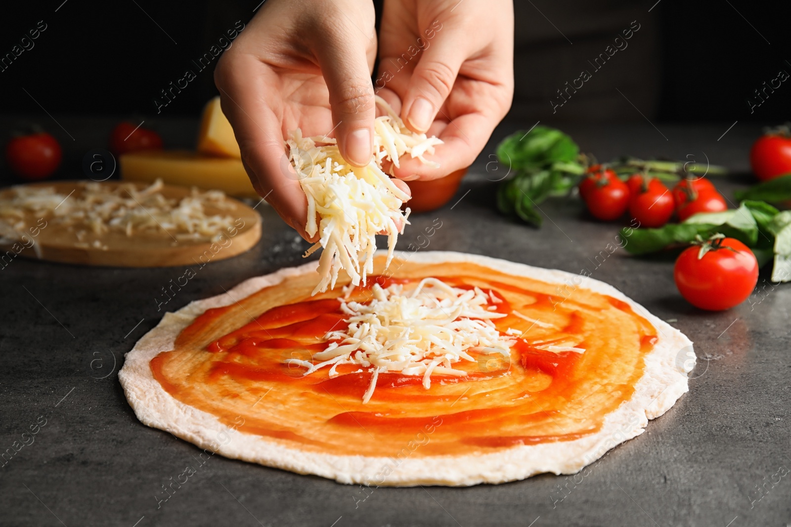 Photo of Woman adding cheese to pizza at grey table, closeup