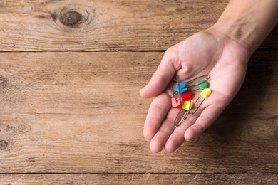 Photo of Woman holding colorful safety pins at wooden table, top view. Space for text