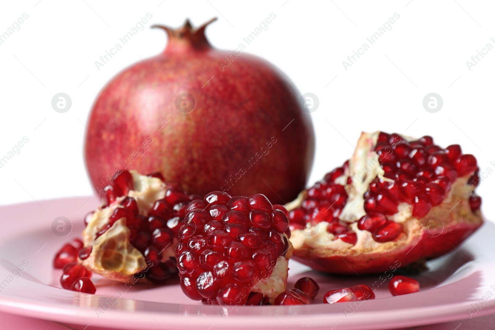 Photo of Plate with ripe pomegranates on table against white background, closeup