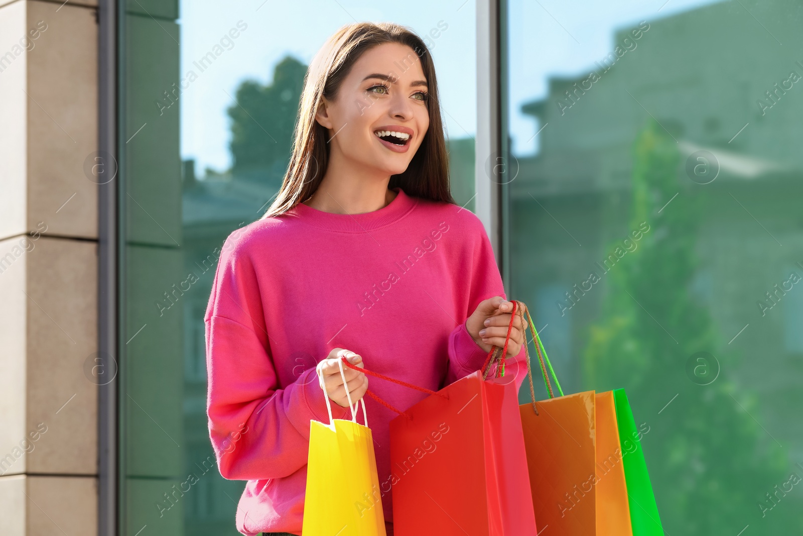 Photo of Beautiful young woman with shopping bags near building outdoors