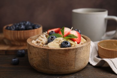 Photo of Tasty oatmeal with strawberries, blueberries and almond flakes in bowl on wooden table, closeup