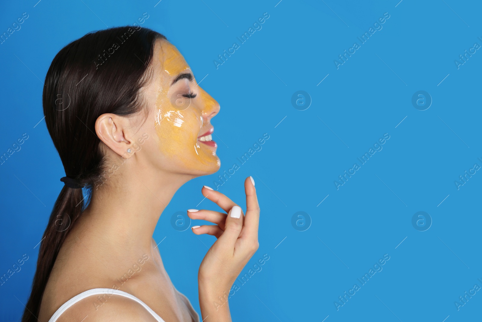 Photo of Young woman with cleansing mask on her face against color background, space for text. Skin care