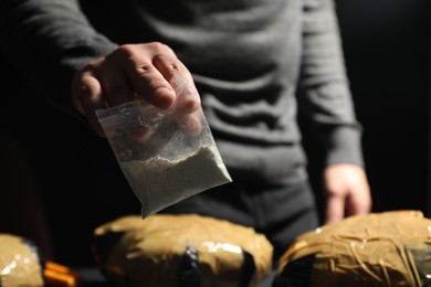 Smuggling and drug trafficking. Man holding plastic bag with cocaine on dark background, closeup