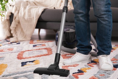 Photo of Man cleaning carpet with vacuum cleaner at home, closeup