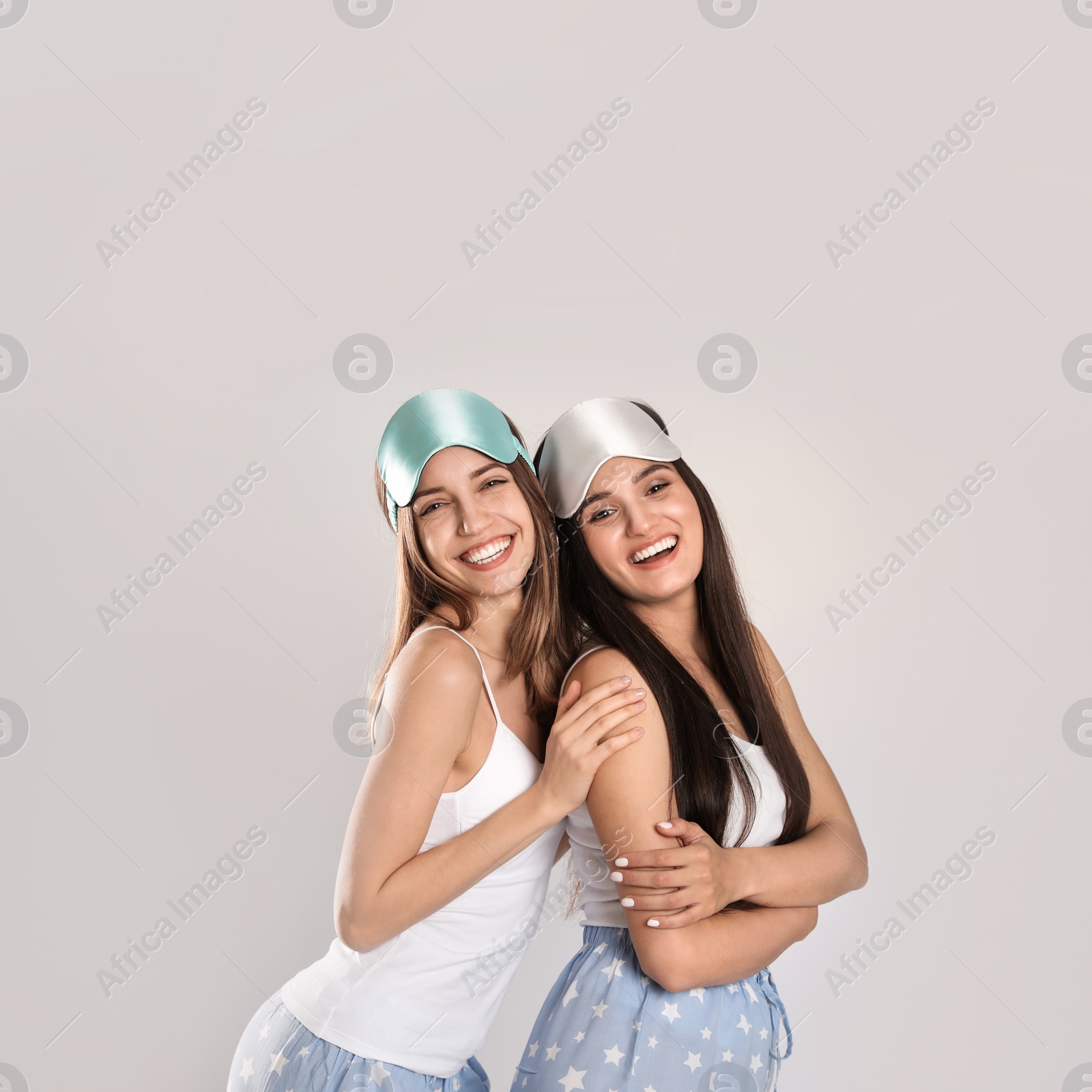 Photo of Beautiful women wearing sleeping masks on light grey background. Bedtime