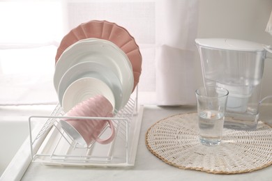 Photo of Drainer with different clean dishware, glass and cup on light table indoors