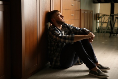 Photo of Depressed young man sitting on floor in kitchen