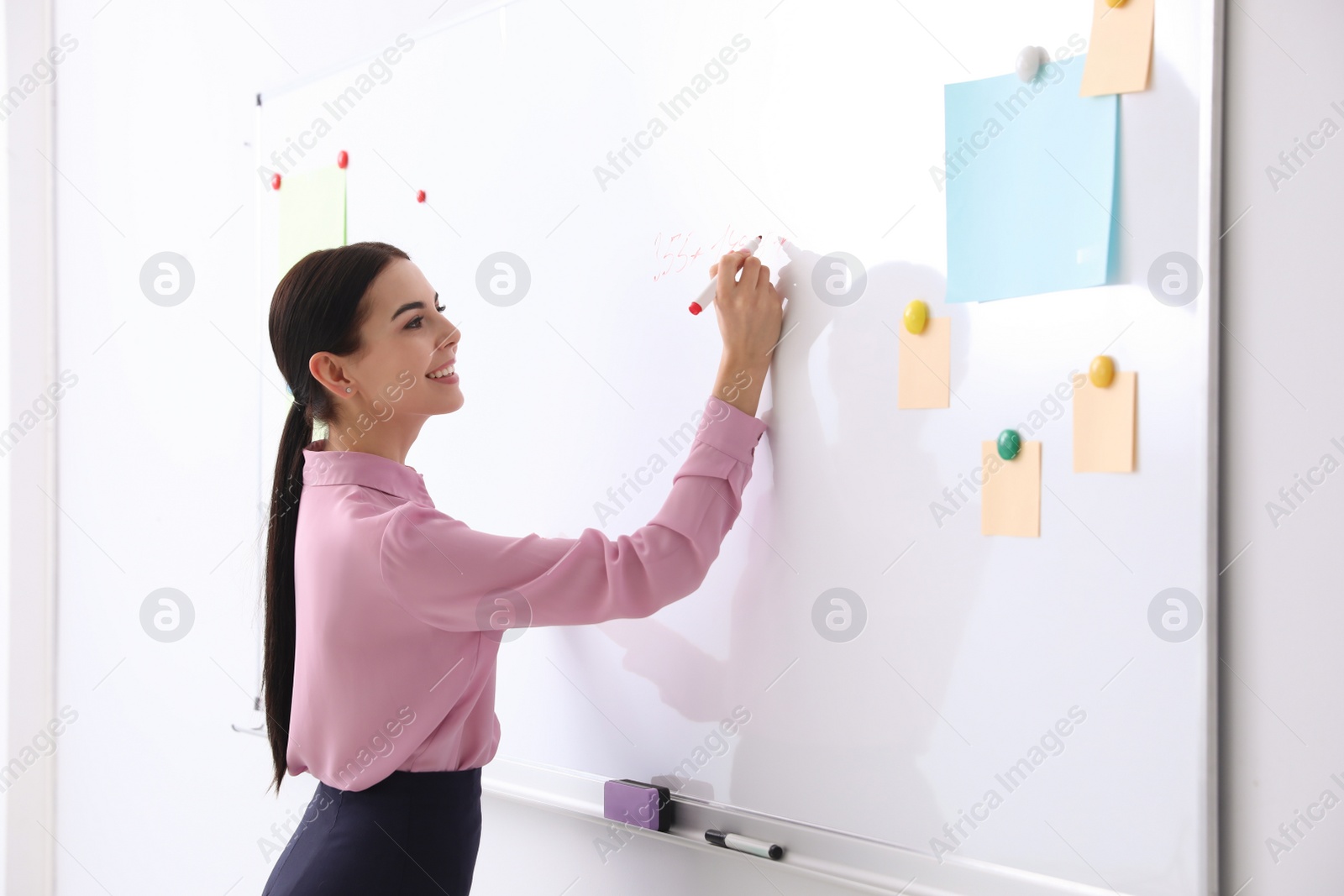 Photo of Young teacher writing on whiteboard in classroom