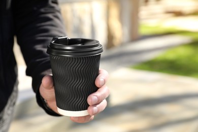 Photo of Man holding paper coffee cup in park, closeup. Space for text