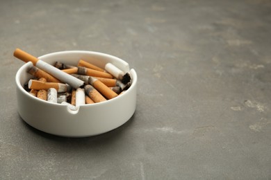 Photo of Ceramic ashtray full of cigarette stubs on grey table. Space for text