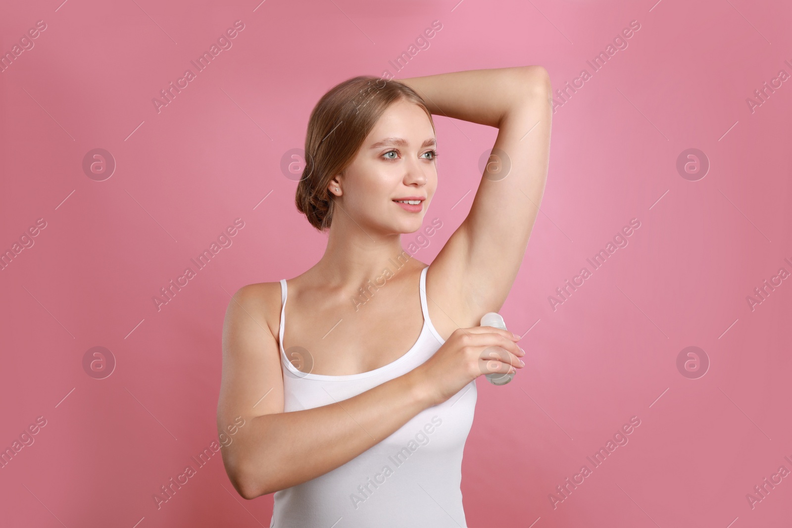 Photo of Young woman applying deodorant to armpit on pink background