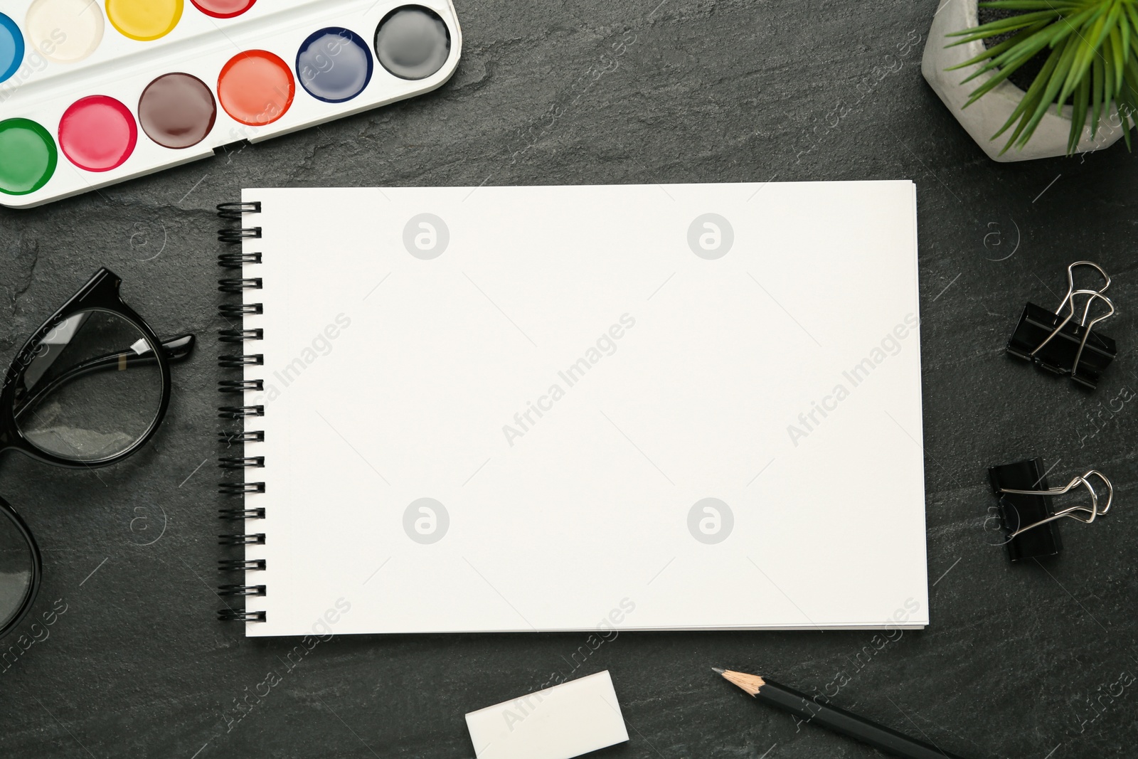 Photo of Flat lay composition with blank sketchbook on black slate table. Space for text