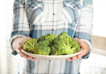 Photo of Woman holding plate with fresh green broccoli in kitchen, closeup
