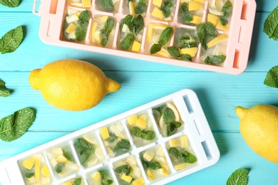 Flat lay composition with ice cube tray, mint and lemons on wooden background