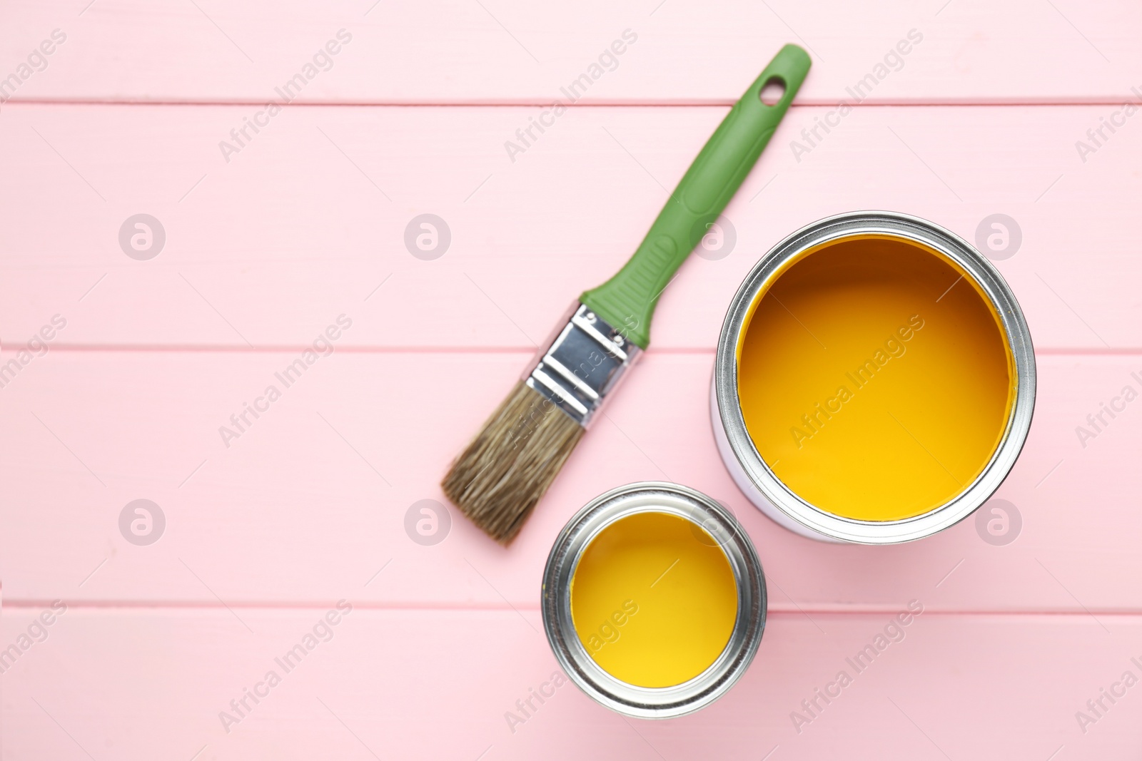 Photo of Cans of yellow paint and brush on pink wooden table, flat lay. Space for text