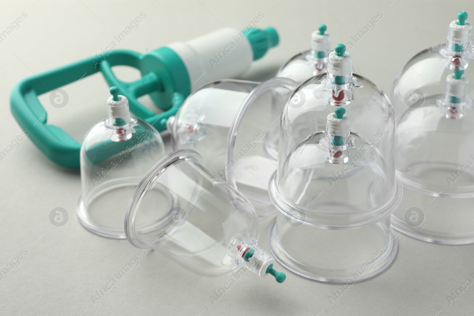 Photo of Plastic cups and hand pump on light grey background, closeup. Cupping therapy