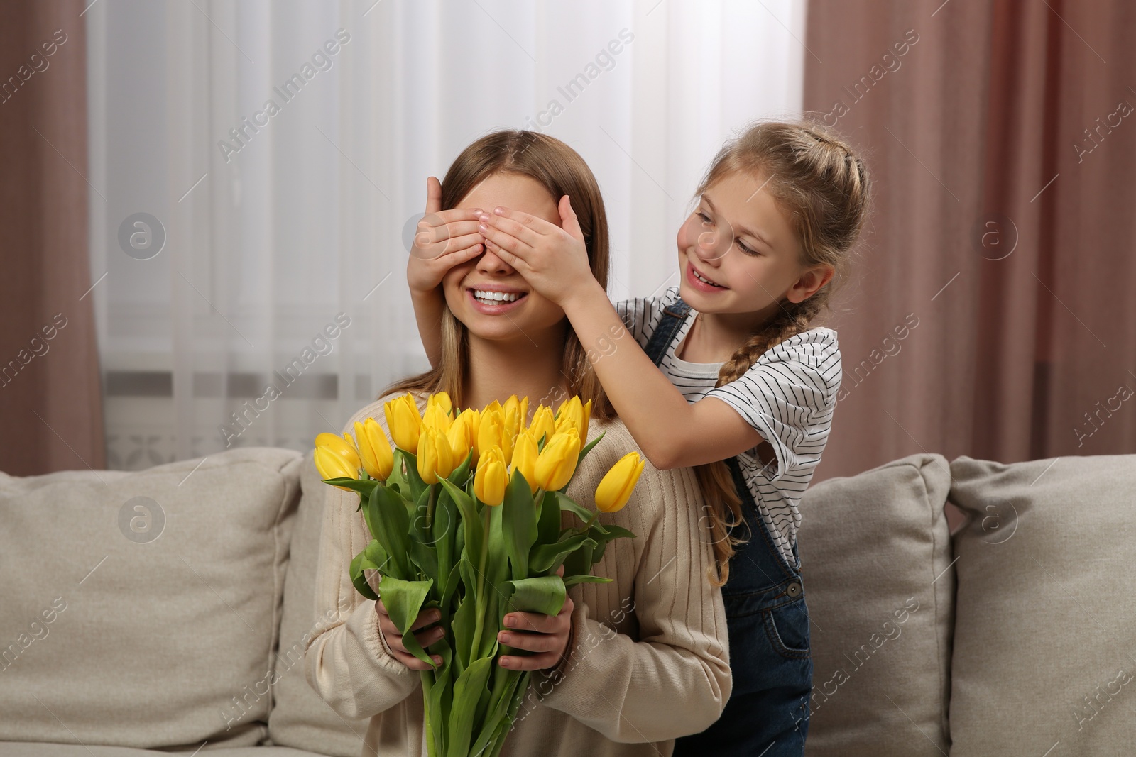 Photo of Little daughter congratulating mom with bouquet of yellow tulips at home. Happy Mother's Day