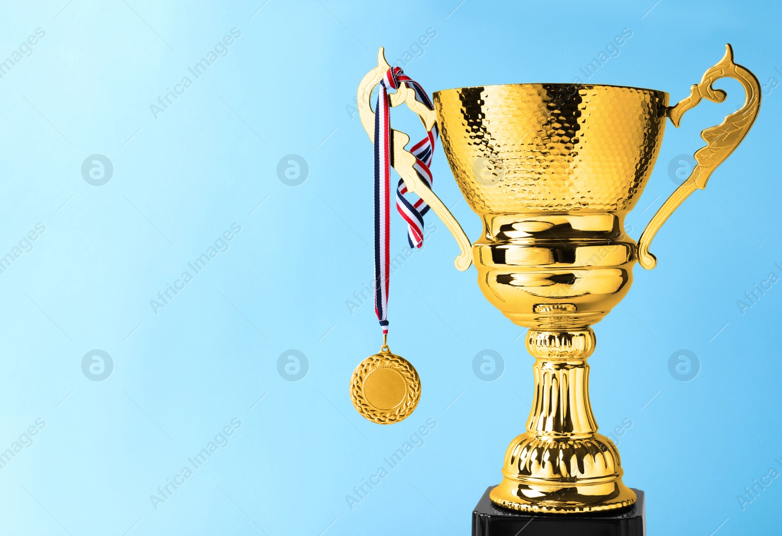 Photo of Golden trophy cup and medal on blue background. Space for text