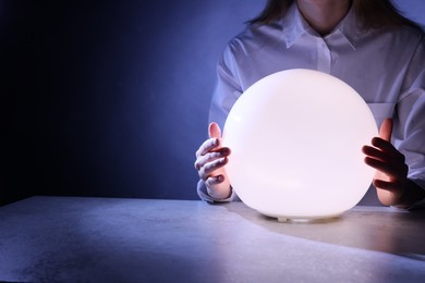 Photo of Businesswoman using glowing crystal ball to predict future at table, closeup. Space for text
