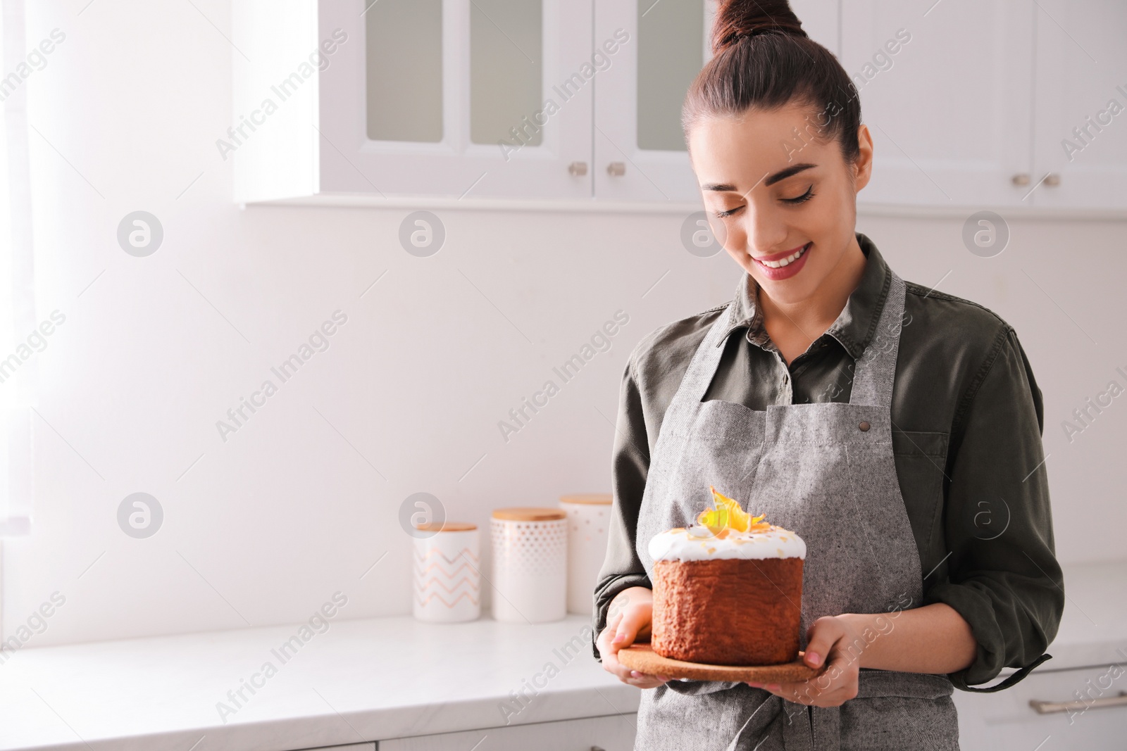 Photo of Young woman with traditional decorated Easter cake in kitchen. Space for text