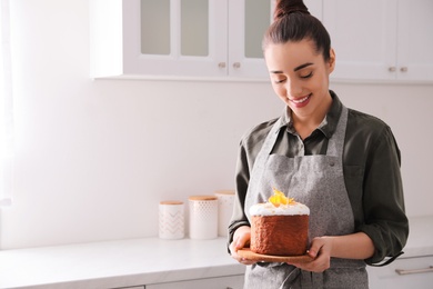 Photo of Young woman with traditional decorated Easter cake in kitchen. Space for text