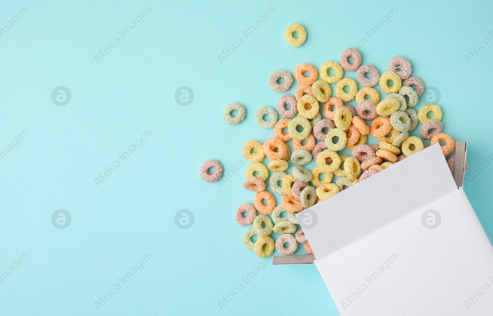 Photo of Paper box with tasty cereal rings on light blue background, flat lay. Space for text