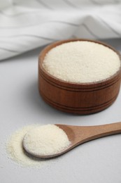 Wooden bowl and spoon with gelatin powder on light grey background