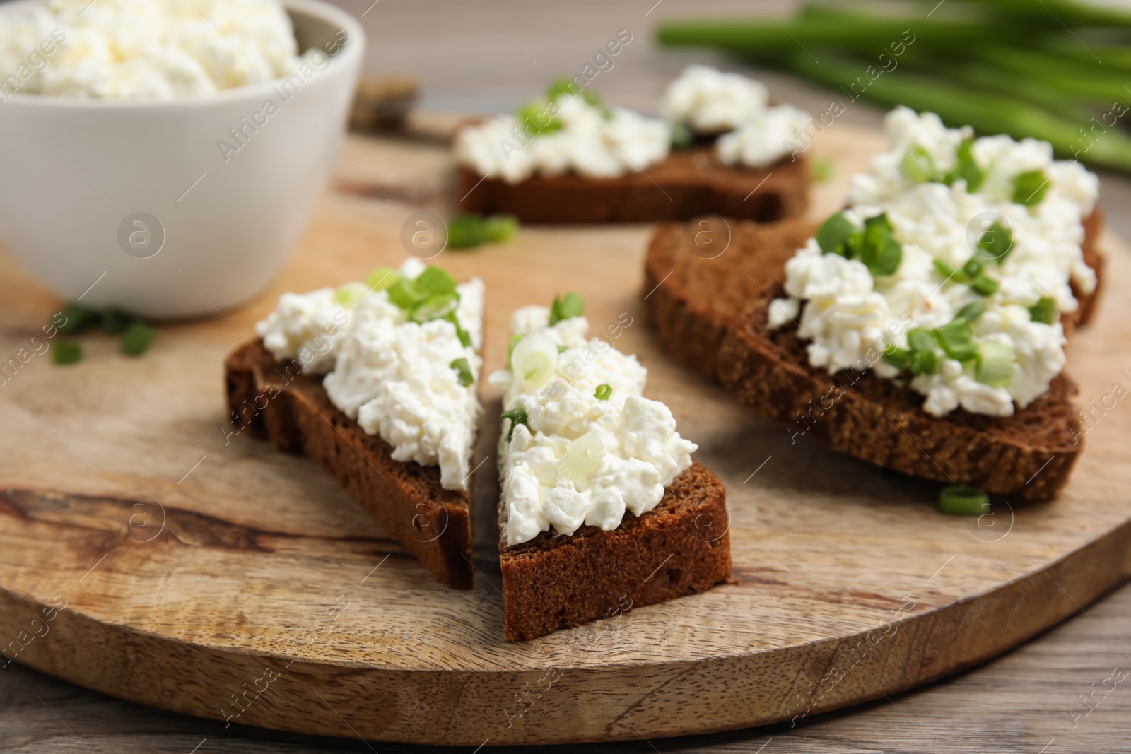 Photo of Bread with cottage cheese and green onion on wooden table, closeup