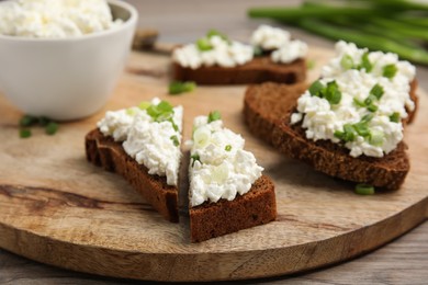 Photo of Bread with cottage cheese and green onion on wooden table, closeup