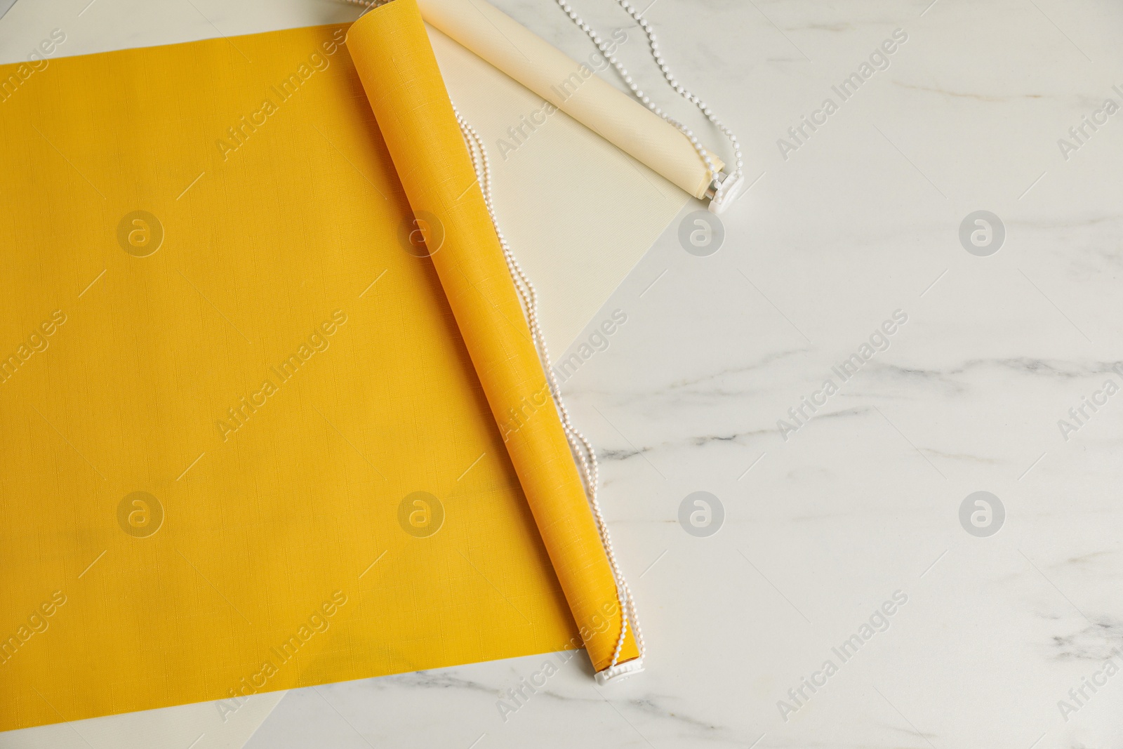 Photo of Stylish roller window blinds on white marble table, flat lay. Space for text