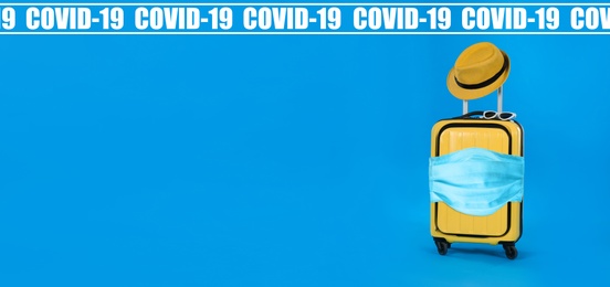 Image of COVID-19 pandemic, travel during coronavirus outbreak. Suitcase with protective mask on blue background, space for text 