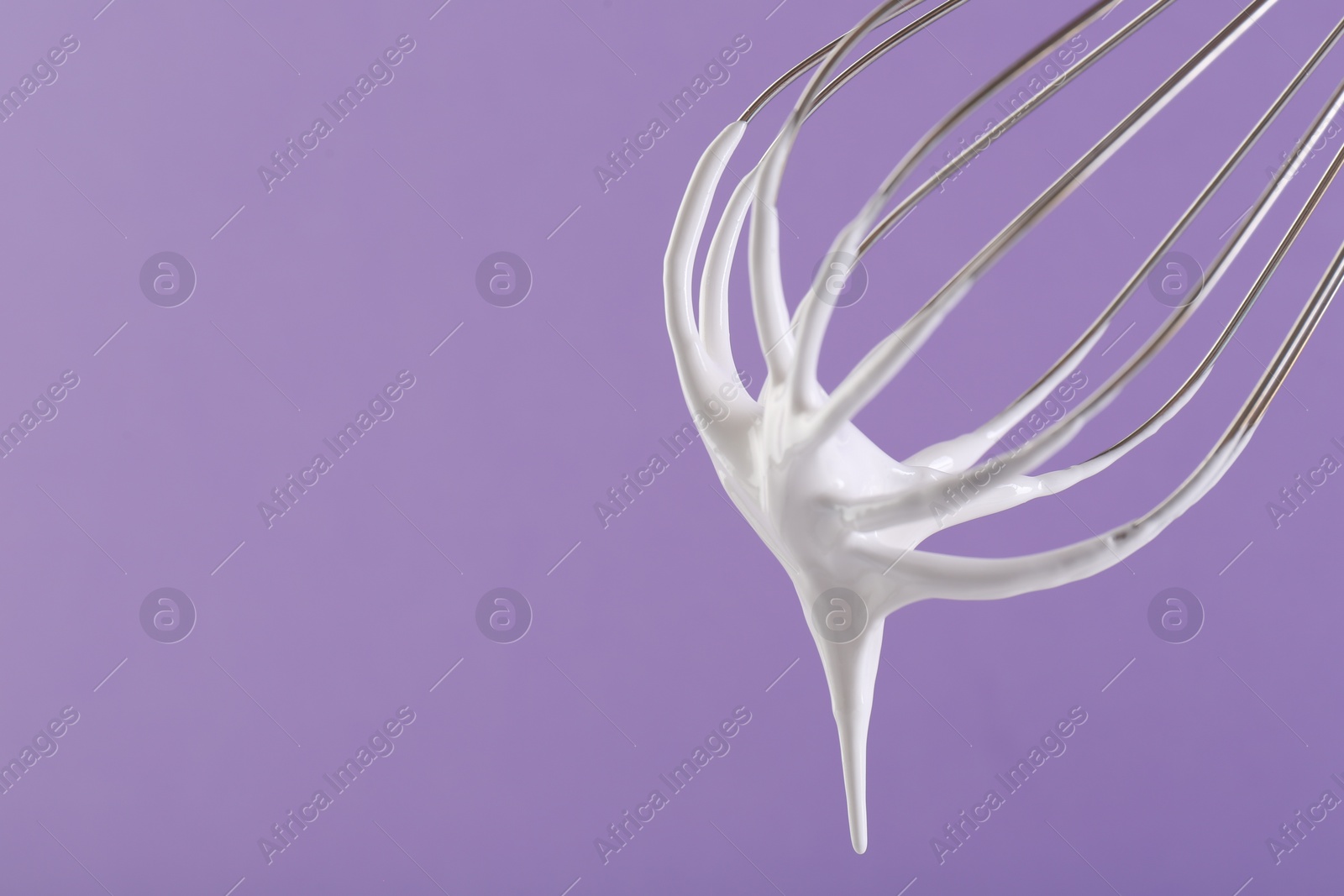 Photo of Whisk with whipped cream on violet background, closeup. Space for text