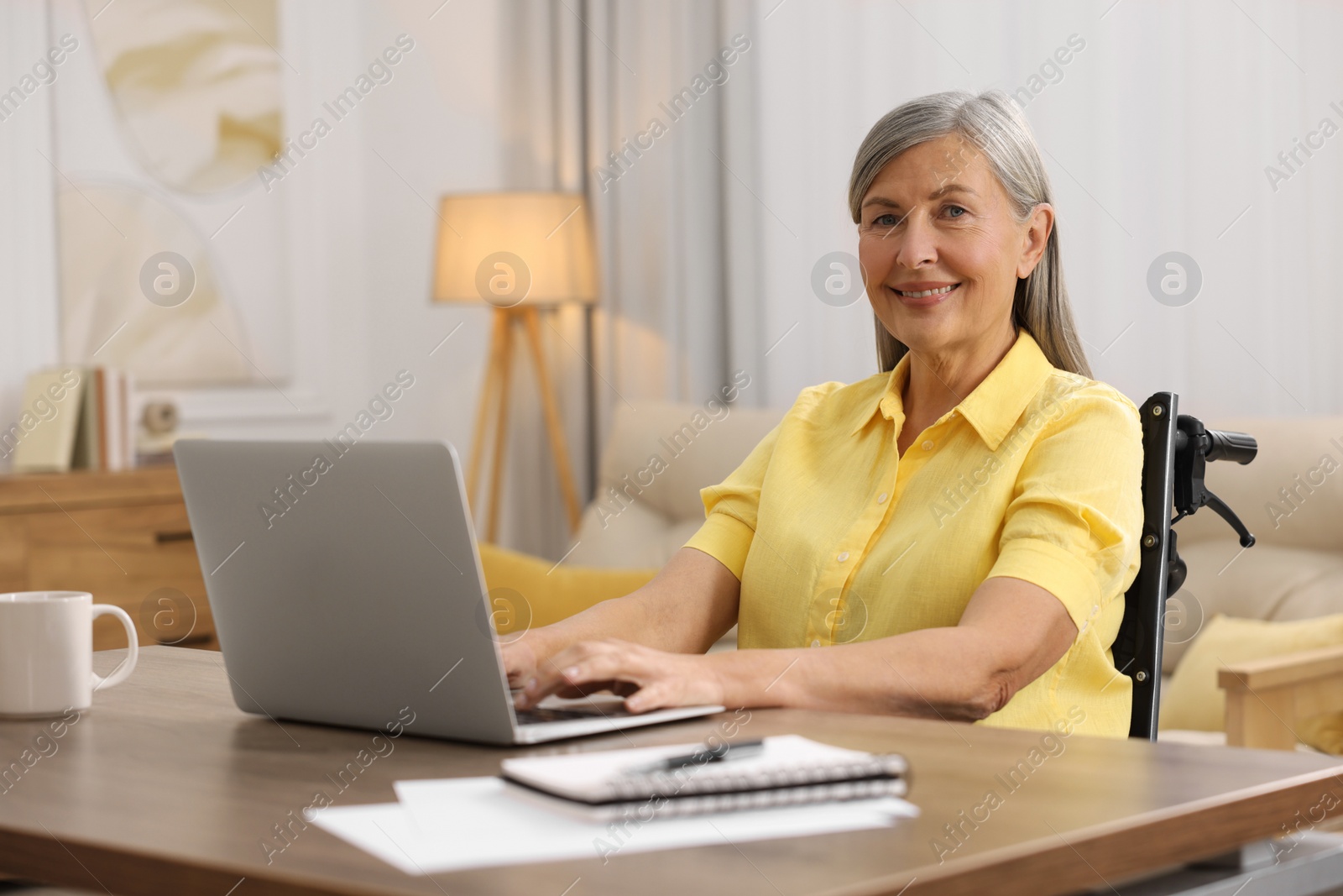 Photo of Woman in wheelchair using laptop at table in home office