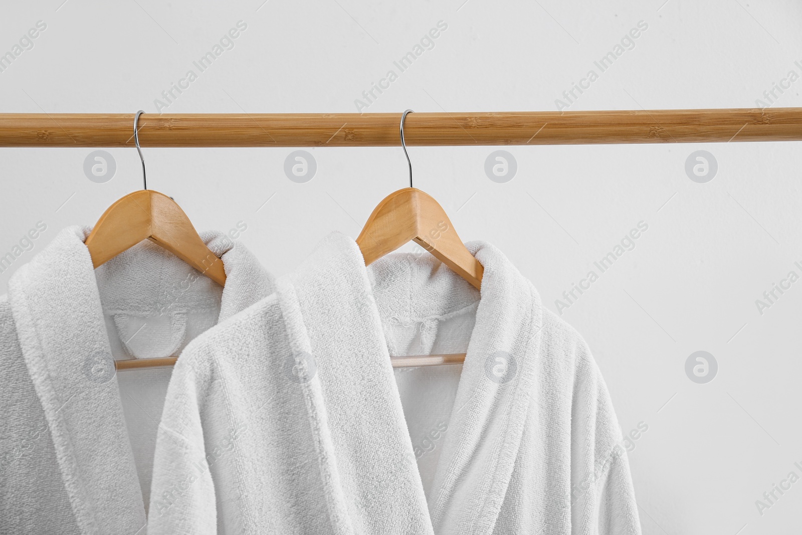 Photo of Fresh bathrobes hanging on rack near white wall