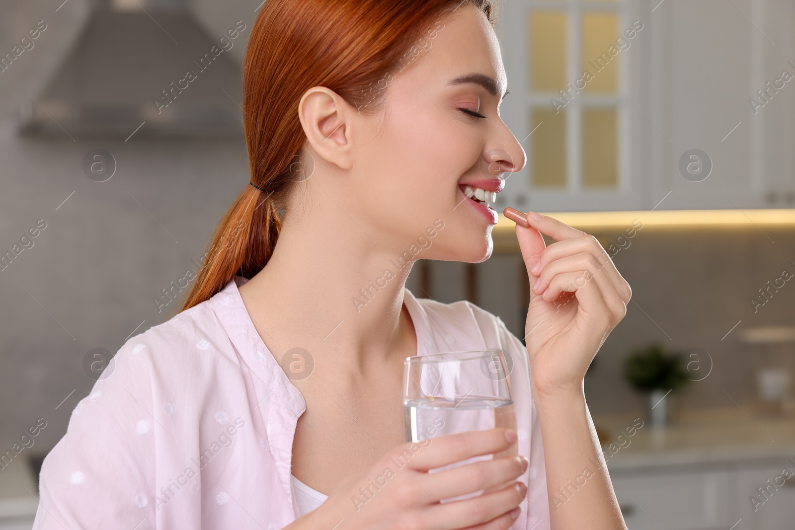 Photo of Beautiful young woman taking vitamin pill at home