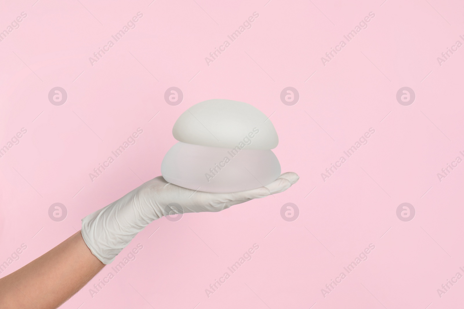 Photo of Doctor holding silicone implants for breast augmentation on color background, space for text. Cosmetic surgery