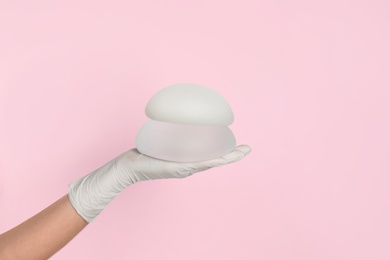 Photo of Doctor holding silicone implants for breast augmentation on color background, space for text. Cosmetic surgery