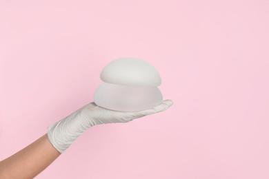 Doctor holding silicone implants for breast augmentation on color background, space for text. Cosmetic surgery