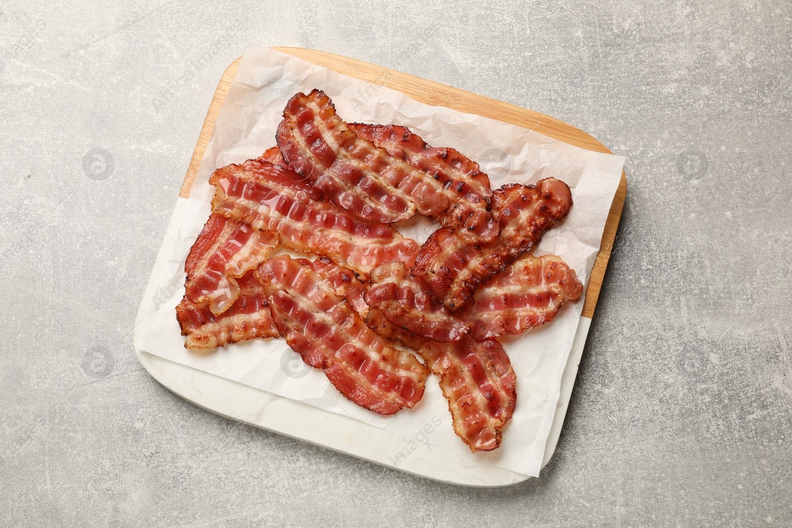 Photo of Board with fried bacon slices on grey textured table, top view