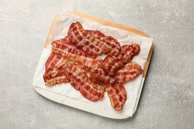 Board with fried bacon slices on grey textured table, top view