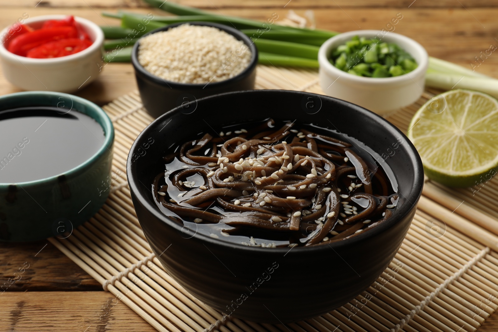 Photo of Tasty soup with buckwheat noodles (soba) and sesame in bowl on wooden table, closeup