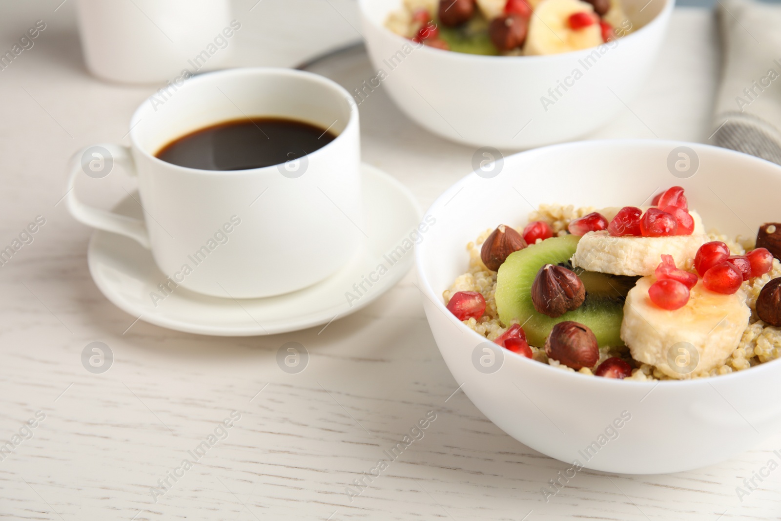 Photo of Quinoa porridge with hazelnuts, kiwi, banana and pomegranate seeds served for breakfast on white wooden table