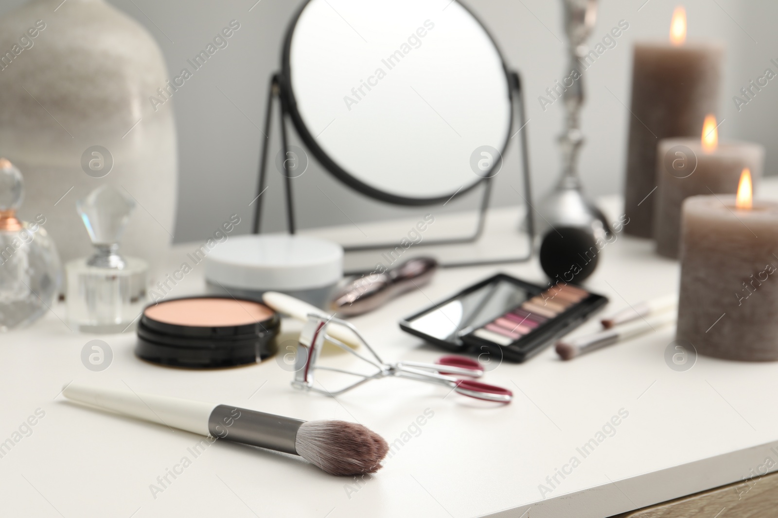 Photo of Brush, mirror, cosmetic products and burning candles on dressing table, closeup