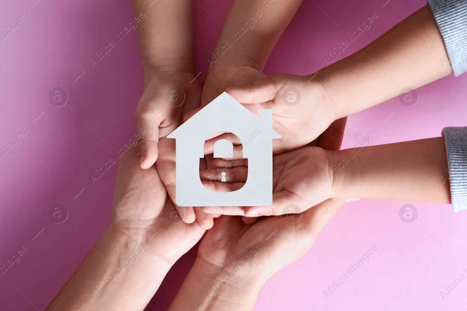 Image of Home security concept. Family holding house on pink background, top view