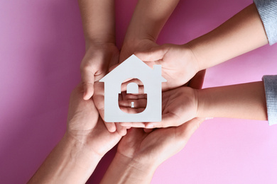 Image of Home security concept. Family holding house on pink background, top view