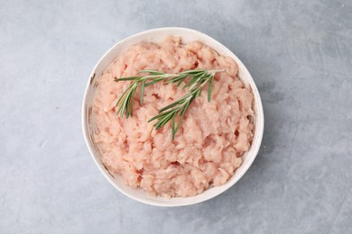 Fresh raw minced meat and rosemary in bowl on light grey textured table, top view