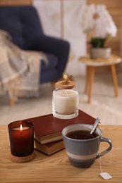 Photo of Cup of tea, books and candles on wooden table in living room. Interior design