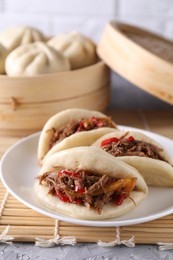 Photo of Plate with delicious gua bao (pork belly buns) on grey textured table, closeup