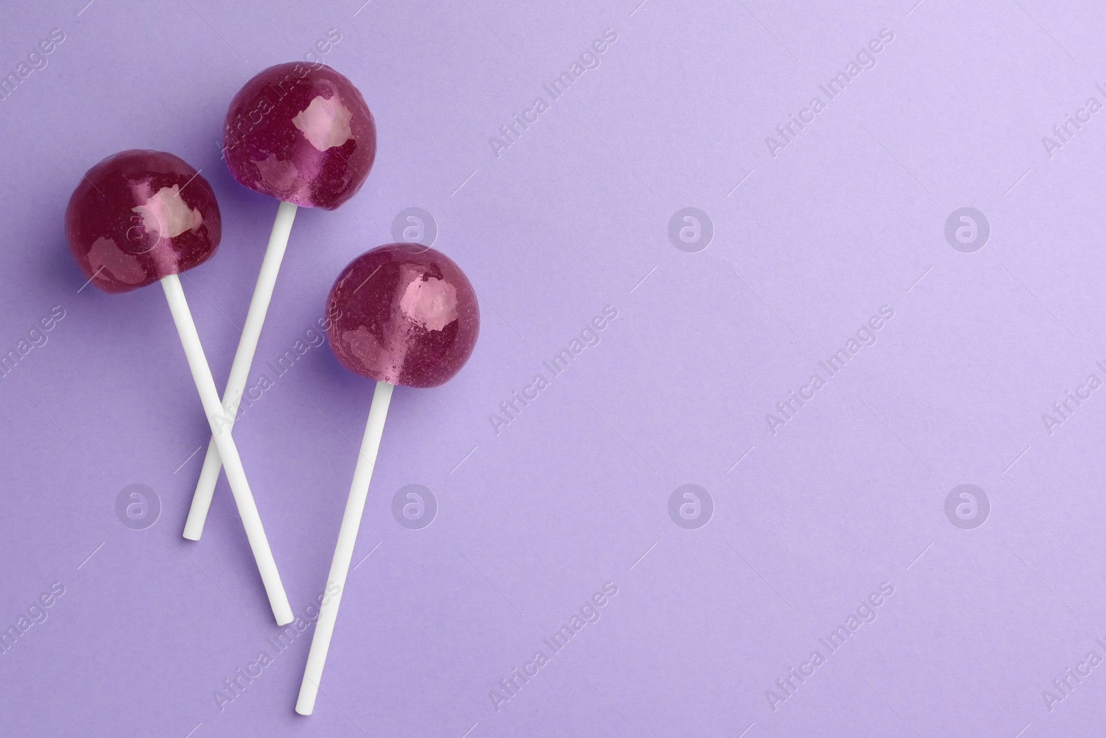 Photo of Tasty lollipops on violet background, flat lay. Space for text