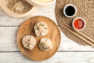 Flat lay composition with tasty baozi dumplings, bamboo steamer and sauces on white wooden table